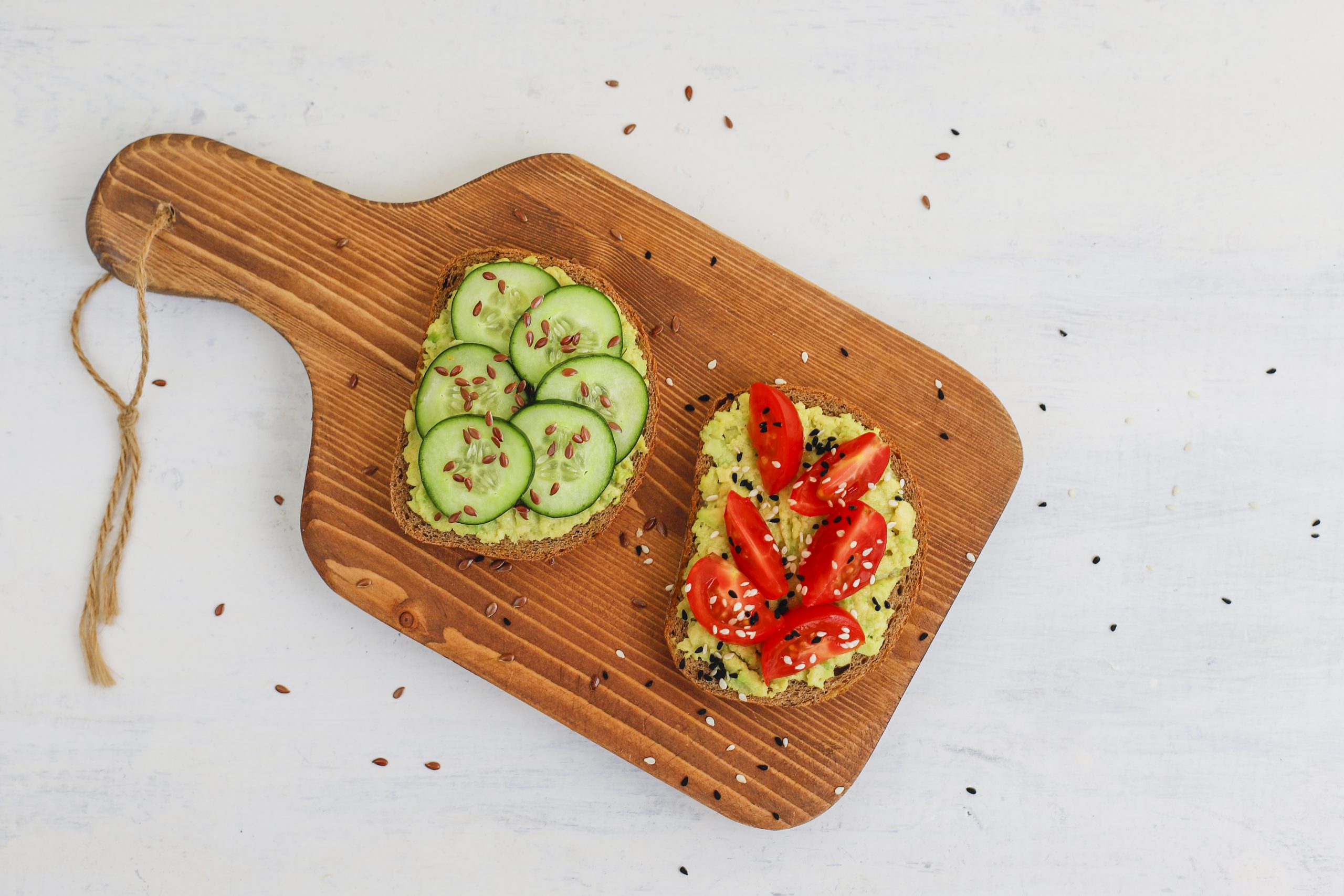 Tostadas de pan integral con aguacate acompañadas de semillas, tomate y pepino,